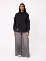 Canguro oversize color negro con efecto lavado, capucha y estampa gráfica en la espalda con tipografía desgastada y detalles en color turquesa.