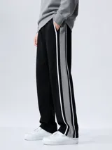 Pantalón de jogging de corte recto, color negro con franjas laterales en gris y líneas blancas. Cuenta con cintura elástica y bolsillos laterales.