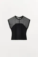 Top combinado de punto color negro, con cuello redondo, manga corta y detalles semitransparentes en la parte superior. Cuenta con costura central marcada en el frente y cierre en la espalda con abertura y botón.