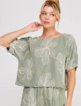 Blusa corta verde militar de lino y viscosa, con cuello redondo y mangas cortas abullonadas con puños elásticos. Presenta grandes flores bordadas en tono claro por toda la prenda.