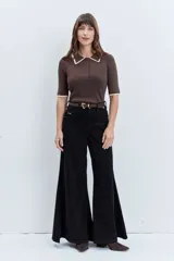 Jeans de tiro alto en color negro, con diseño de corte acampanado y paneles godet que aportan amplitud en el bajo. Presenta costuras visibles y cierre frontal con botón y cremallera.