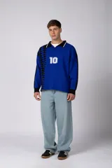 Camiseta de tejido de punto con cuello polo, manga larga y diseño inspirado en camisetas de fútbol retro. Presenta un color azul vibrante con un patrón geométrico lateral en negro y el número 10 estampado en el frente.