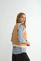Chaleco de punto con diseño a rayas horizontales en gris y blanco. Presenta cuello redondo, bordes y bolsillos frontales con detalles en color rojo, y cierre frontal con botones rojos.