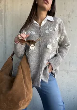 Cardigan de punto color beige con diseño de flores bordadas en relieve, cuello redondo, cierre frontal con botones y puños acanalados.
