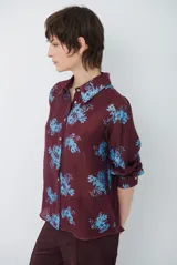 Camisa de corte clásico con cuello camisero y cierre frontal de botones, confeccionada en tela color bordó con estampado floral en tonos celestes.