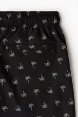 Short de baño negro de sirsaca con estampado de palmeras blancas, cintura elástica con cordón de ajuste blanco y bolsillos laterales.