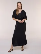Vestido largo amarillo de corte fluido con escote en V, mangas cortas amplias y apliques de tachas en el escote y puños. Posee cintura elastizada fruncida y falda larga con tajos laterales en el ruedo.