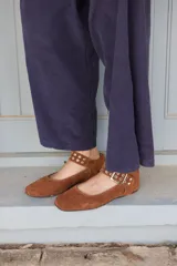 Ballerina de gamuza color marrón, con tira ajustable en el empeine que incluye hebilla metálica y detalles de ojales plateados.