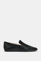 Zapato tipo mocasín de piel negra con copete subido, punta redonda y suela plana.