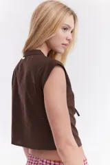 Blusa sin mangas de algodón con estampado de rayas en tonos beige, azul y rojo. Presenta diseño de inspiración oriental con cierre frontal de múltiples lazos para atar.