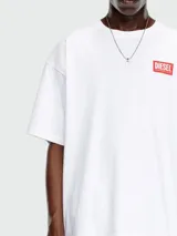 Remera blanca de corte holgado con cuello redondo y manga corta. Presenta un pequeño parche rectangular rojo con el logo de Diesel en el pecho.