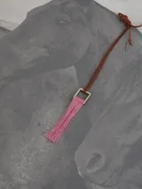 Collar largo con cordón de cuero marrón, dije cuadrado metálico plateado y borla de hilos en color rosado.