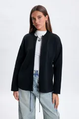 Campera de punto color negro con cierre frontal, cuello redondo y mangas largas. Presenta un diseño minimalista y versátil con cordones ajustables en la parte inferior.