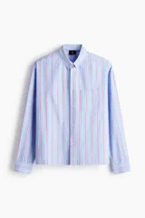 Camisa de corte relajado confeccionada en algodón, con diseño de rayas verticales en tonos azul, blanco y rojo. Presenta cuello americano, cierre frontal con botones, bolsillo en el pecho y mangas largas con puños abotonados.