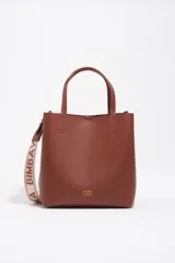 Bolso de hombro de tamaño mediano color marrón, confeccionado en piel vacuna. Presenta doble asa corta de mano y correa de tejido jaspeada con el nombre de la marca estampado. Incluye detalles en piel, cierre con botón de presión, logo grabado en dorado en el frente y acabados metálicos.