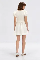 Vestido corto blanco de viscosa con mangas cortas abullonadas, cuerpo con punto smock y tiras para anudar en el escote en V, y falda evasé.