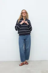 Sweater de punto azul marino con rayas horizontales blancas, cuello alto con cierre frontal y manga larga de diseño holgado.