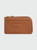 Tarjetero Longchamp de la línea Le Foulonné, confeccionado en cuero vacuno granulado color tostado. Presenta cierre superior con cremallera metálica dorada y logo de la marca grabado en el frente.
