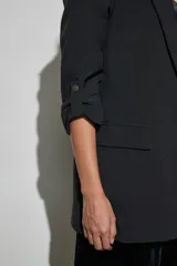 Blazer negro de corte recto con solapa clásica y mangas tres cuartos con detalles de trabilla y botón metálico.