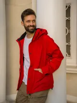 Campera rompevientos roja con capucha, cierre frontal con botones a presión y bolsillos laterales con solapa. Interior del cuello en contraste negro.
