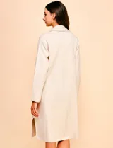 Cardigan largo de tejido color beige claro, sin cuello, con bolsillos frontales y detalles de pespuntes decorativos a lo largo del borde frontal.