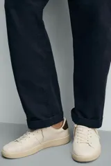 Zapatilla deportiva de diseño minimalista en color crema, con detalle de contraste en color marrón oscuro en el talón y suela de goma con volumen.