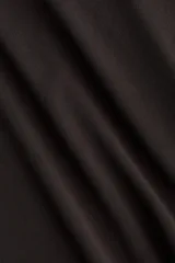 Top de manga corta color marrón oscuro con escote redondo y diseño drapeado en el hombro y panel frontal cruzado que crea una silueta asimétrica.