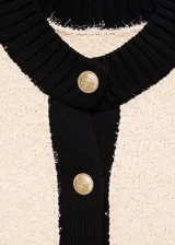 Chaqueta de punto de textura suave en color crema con detalles en contraste negro en cuello, puños, ruedo y tapeta de botones. Presenta un diseño recto, cuello redondo y cierre frontal con botones dorados.