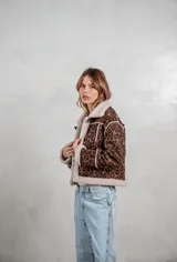 Campera de gamuza con estampado animal print de leopardo, forrada en corderito sintético color crema. Presenta cierre frontal con botones tipo toggle, cuello solapa y detalles de costuras visibles.