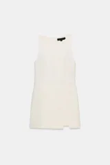 Mono corto color blanco hueso, sin mangas, con cuello redondo y detalle de cruce o abertura en la parte delantera inferior. Cierre con cremallera oculta en la espalda.