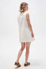 Vestido corto de jean blanco con tirantes anchos, cuello redondo, corte holgado y bolsillos laterales.