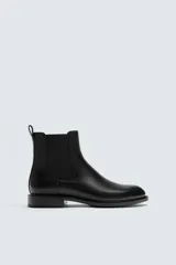Bota estilo Chelsea de cuero negro con diseño liso, paneles elásticos laterales y tirador trasero. Presenta horma redonda y suela con tacón bajo.