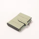 Billetera compacta color verde menta, con cierre de solapa y broche a presión. Presenta detalles de costuras decorativas en color beige en el frente y un bolsillo exterior con cierre.