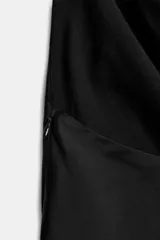 Top negro de tejido satinado con cuello halter que cae en un escote pronunciado y fluido. Presenta tiras largas que caen al frente, adornadas con abalorios brillantes.