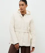 Campera acolchada de microfibra color crema, con diseño capitoneado, capucha integrada, cierre frontal oculto y cinturón ajustable del mismo tejido para entallar la silueta.