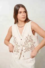 Chaleco de muselina color beige con diseño bordado marrón en la parte delantera, escote en V y cierre frontal de botones.