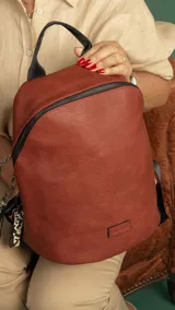 Mochila de símil cuero color negro, con asa de mano superior y correas regulables para llevar al hombro. Presenta cierre principal curvo en la parte superior y un bolsillo oculto en la espalda. Incluye llaveros colgantes decorativos en el tirador del cierre principal.