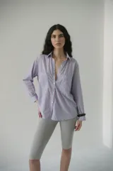 Camisa de rayas verticales rosadas y celestes, con cuello clásico, botonadura frontal y doble bolsillo delantero. Tiene un calce relajado y terminación curva en el ruedo.