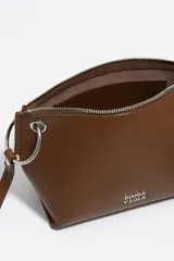 Bolso bandolera de piel vacuna color marrón, con forma trapezoidal y estructura rígida. Posee asa regulable de piel, cierre de cremallera y un detalle de borla multicolor en uno de los laterales.