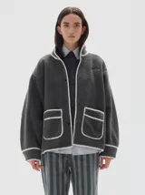 Campera de sherpa color gris oscuro con vivos en color blanco. Presenta cuello alto, cierre frontal con broches a presión, mangas largas y dos bolsillos frontales con ribetes a contratono.