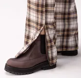 Botas tipo chelsea de cuero marrón con suela track de goma negra. Presentan una combinación de texturas en el cuero y elásticos laterales negros.