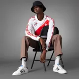 Camiseta de fútbol Adidas de manga larga de River Plate, modelo retro inspirado en 1994. Diseño en color blanco con la tradicional banda roja diagonal, cuello polo, y detalles en rojo en los hombros y las icónicas tres tiras en las mangas.