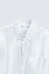 Camisa celeste a rayas verticales, de corte relaxed fit, confeccionada en lino y algodón. Tiene cuello abotonado, manga larga con puños abotonados, bolsillo de parche en el pecho y cierre frontal con botones.