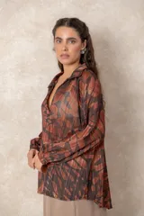 Blusa de gasa con estampado abstracto en tonos verdes y marrones, con detalles de hilos dorados. Presenta cuello camisero con escote en V, mangas largas con puños elásticos y un corte holgado.