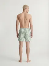 Short de baño de color verde con estampado geométrico de líneas blancas, cintura elástica con cordón de ajuste y bolsillos delanteros.