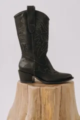 Botas tejanas de cuero negro con caña alta, taco cuadrado y delicadas costuras en contraste que forman diseños bordados en el cuerpo y empeine.