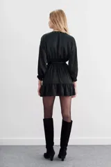 Vestido corto de estilo cruzado, color negro, con mangas largas abullonadas, puños elásticos y volado en el ruedo. Presenta un diseño de jacquard con corazones y cierre frontal con botones metálicos.