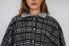 Poncho de paño con estampa a cuadros en tonos grises, negros y blancos, con cuello camisero gris y cierre frontal con dos botones.