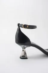 Sandalias negras con punta cuadrada, tira delantera fina y pulsera ajustable al tobillo. Destacan por su taco geométrico transparente de altura media.