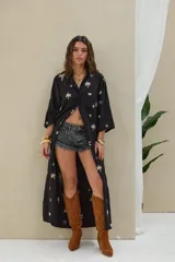 Camisola larga de color negro con bordados en tono beige de palmeras, soles y conchas. Cuenta con cuello camisero, cierre frontal con botones, mangas largas y bolsillos frontales.